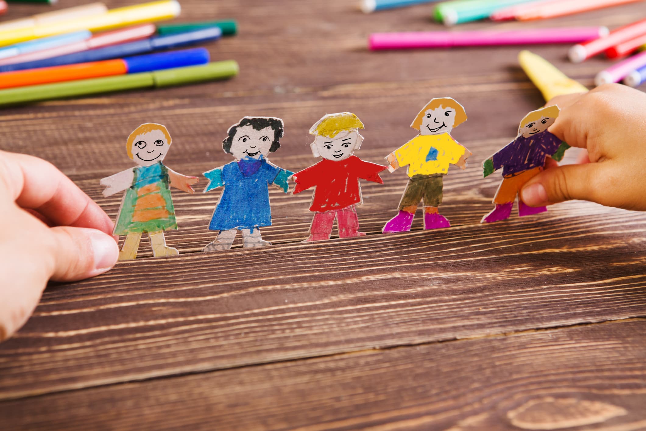Paper cutout figures of children holding hands on a table with markers